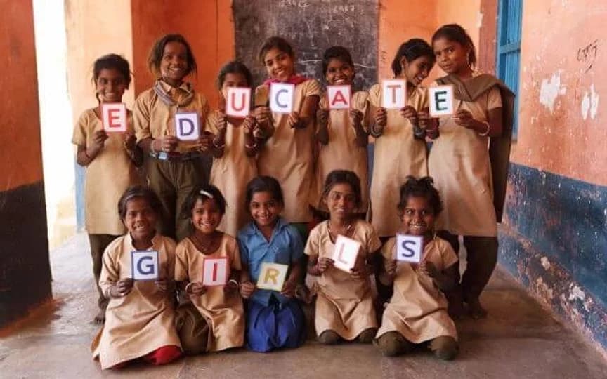 Schoolgirls in uniform hold up letter cards that spell Educate Girls
